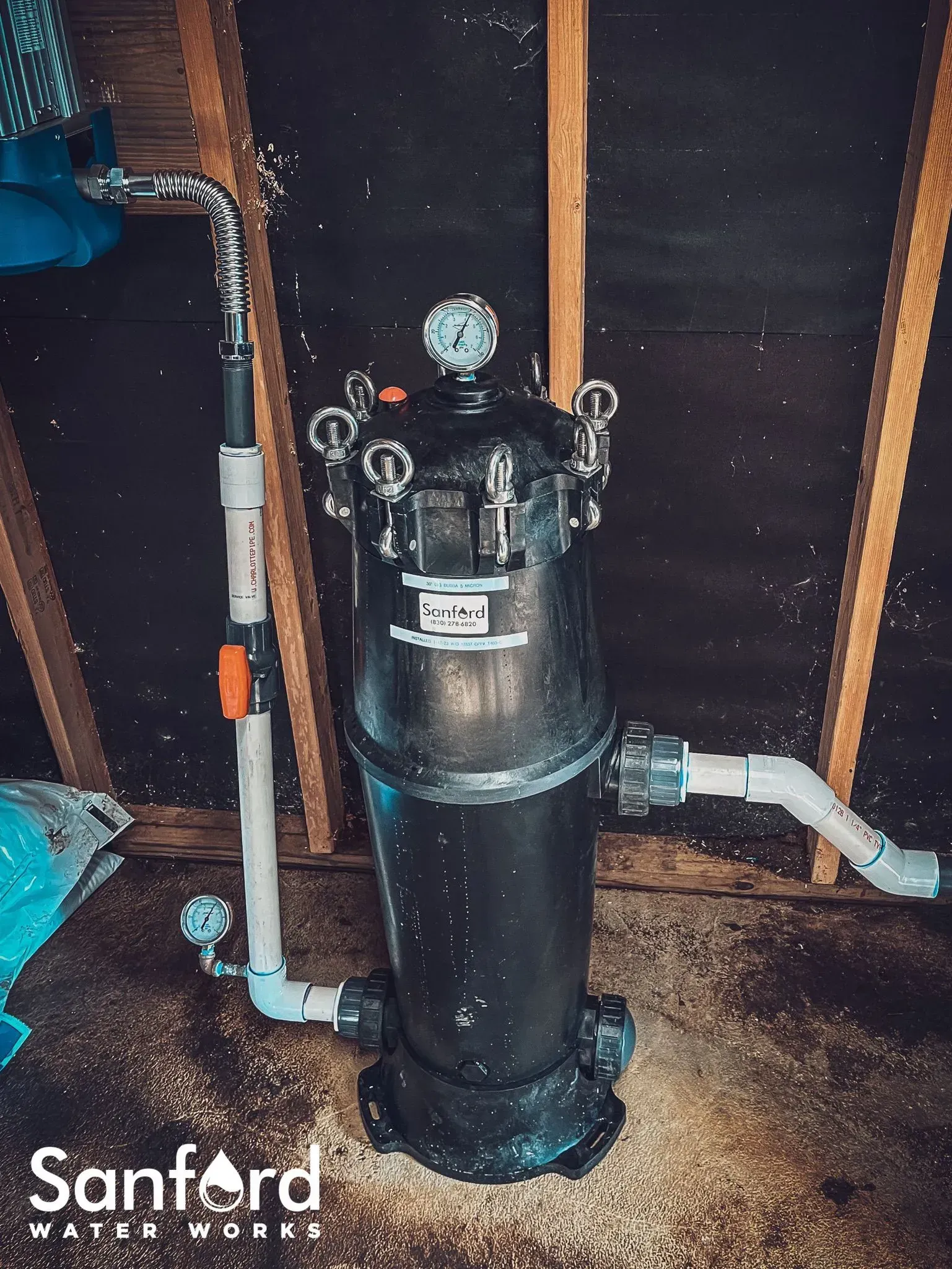 Black water filtration system in an attic, with pipes and a pressure gauge.