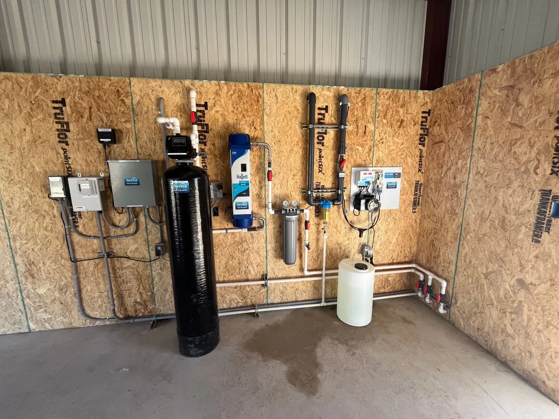 Water filtration system installed on a wood-paneled wall inside a room, with various pipes and tanks.