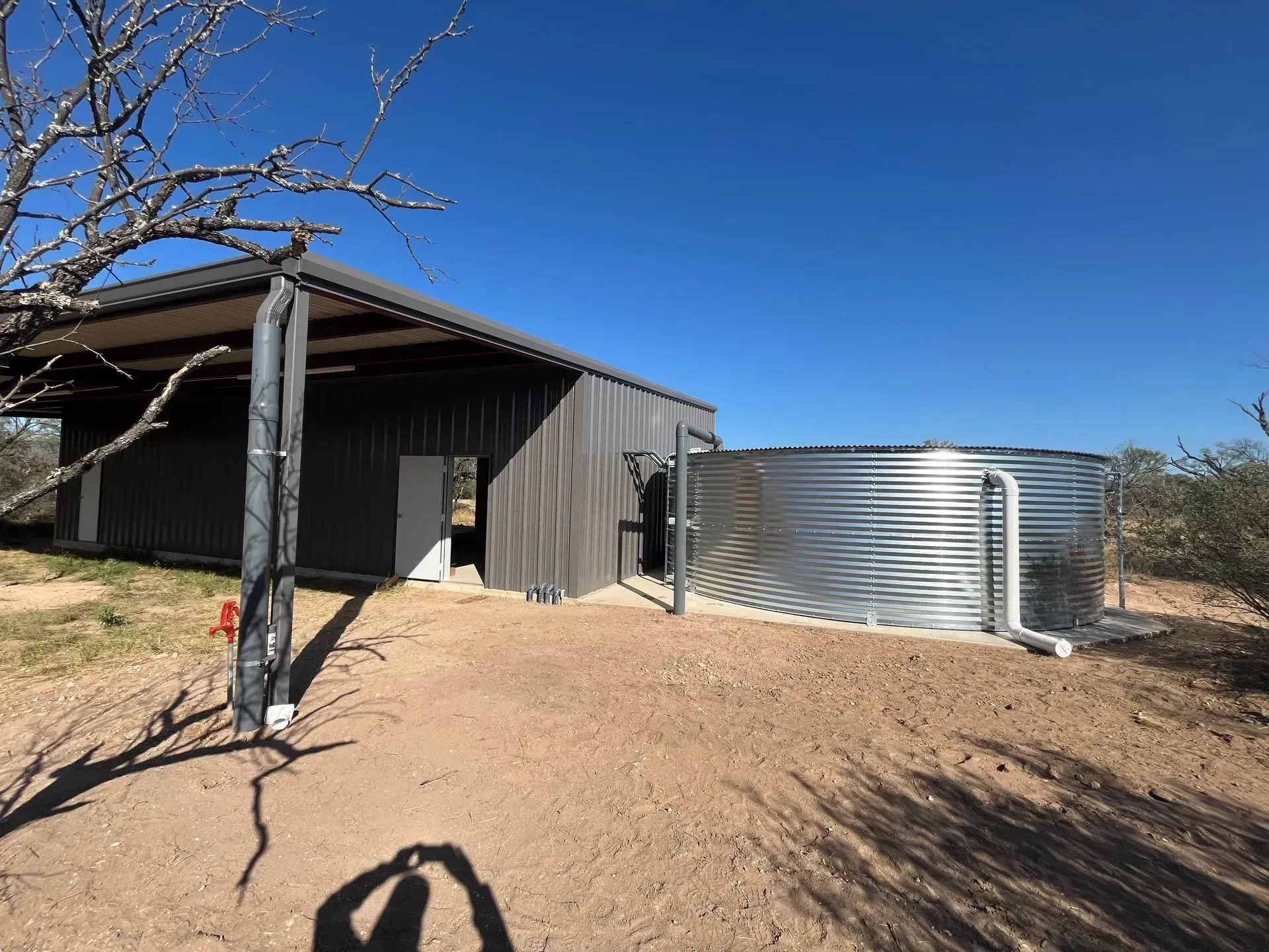 A corrugated metal water tank next to a dark gray shed under a bright blue sky.