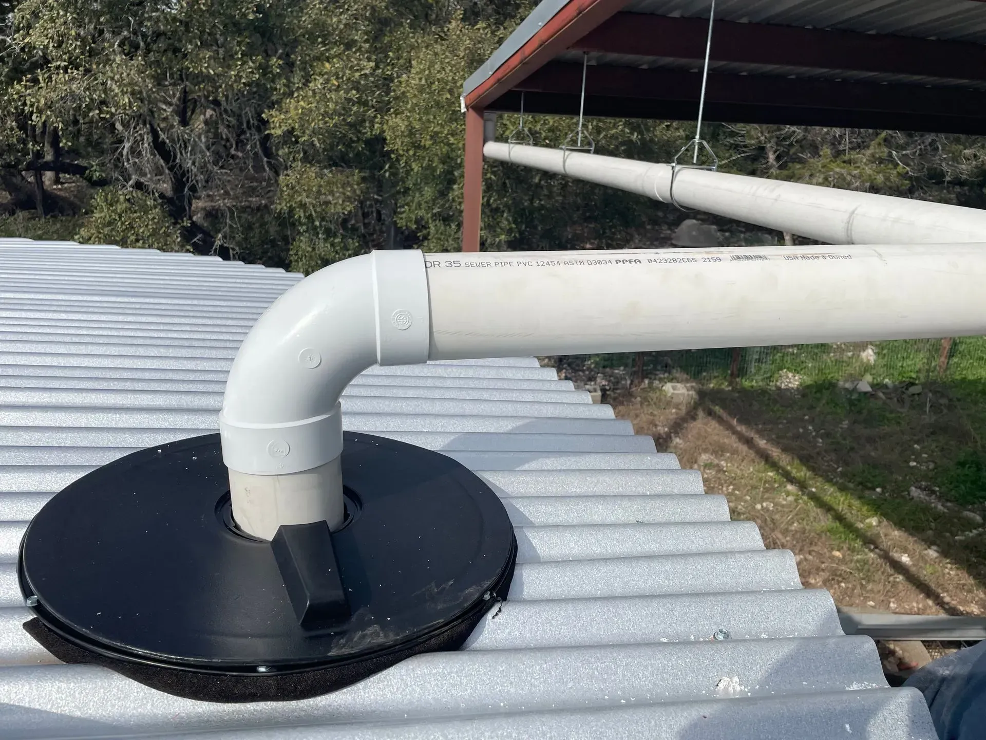 White PVC pipe attached to a corrugated metal roof with a black sealing base.
