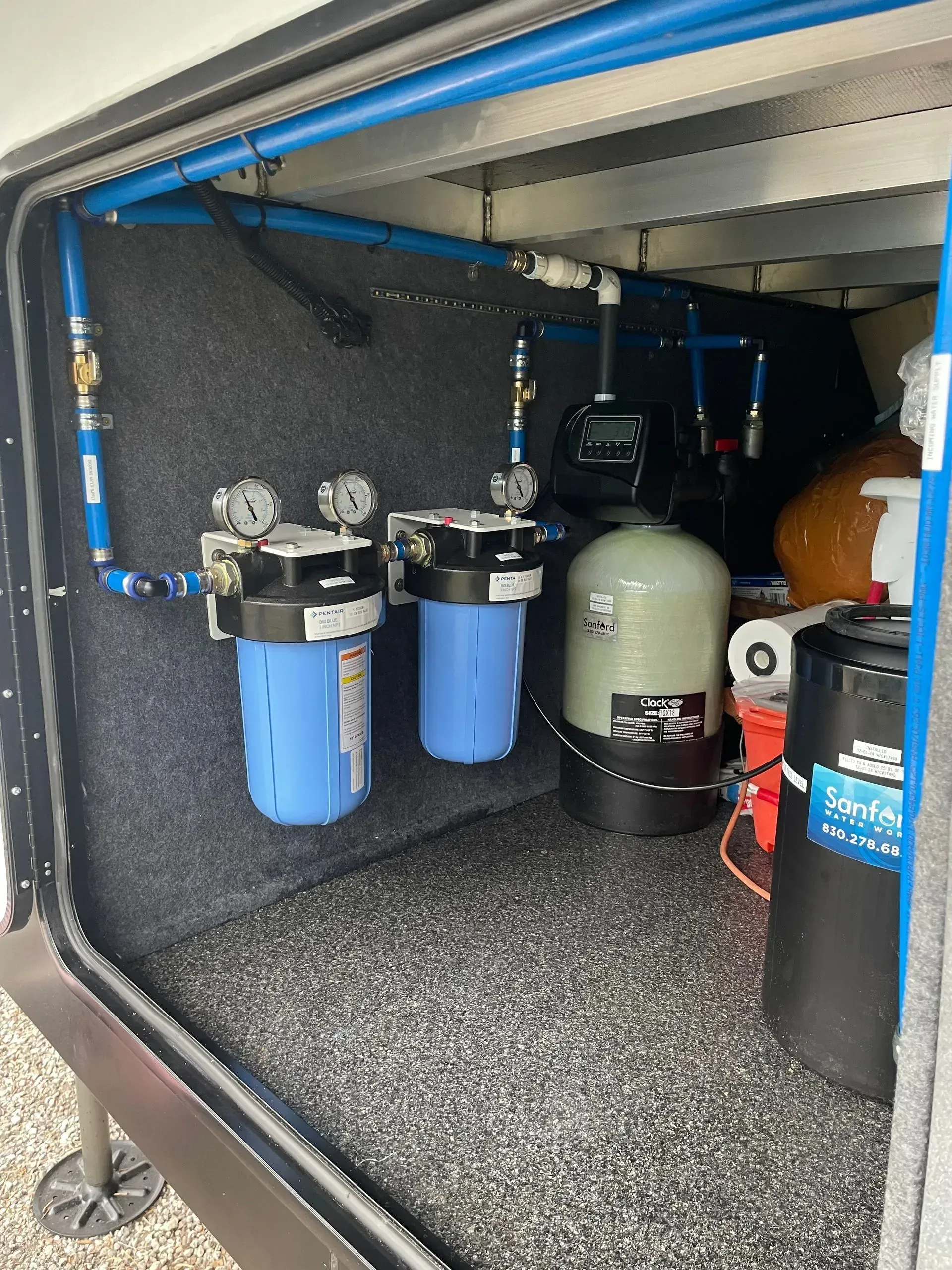 RV water filtration system with blue filters, tanks, and piping in a compartment.