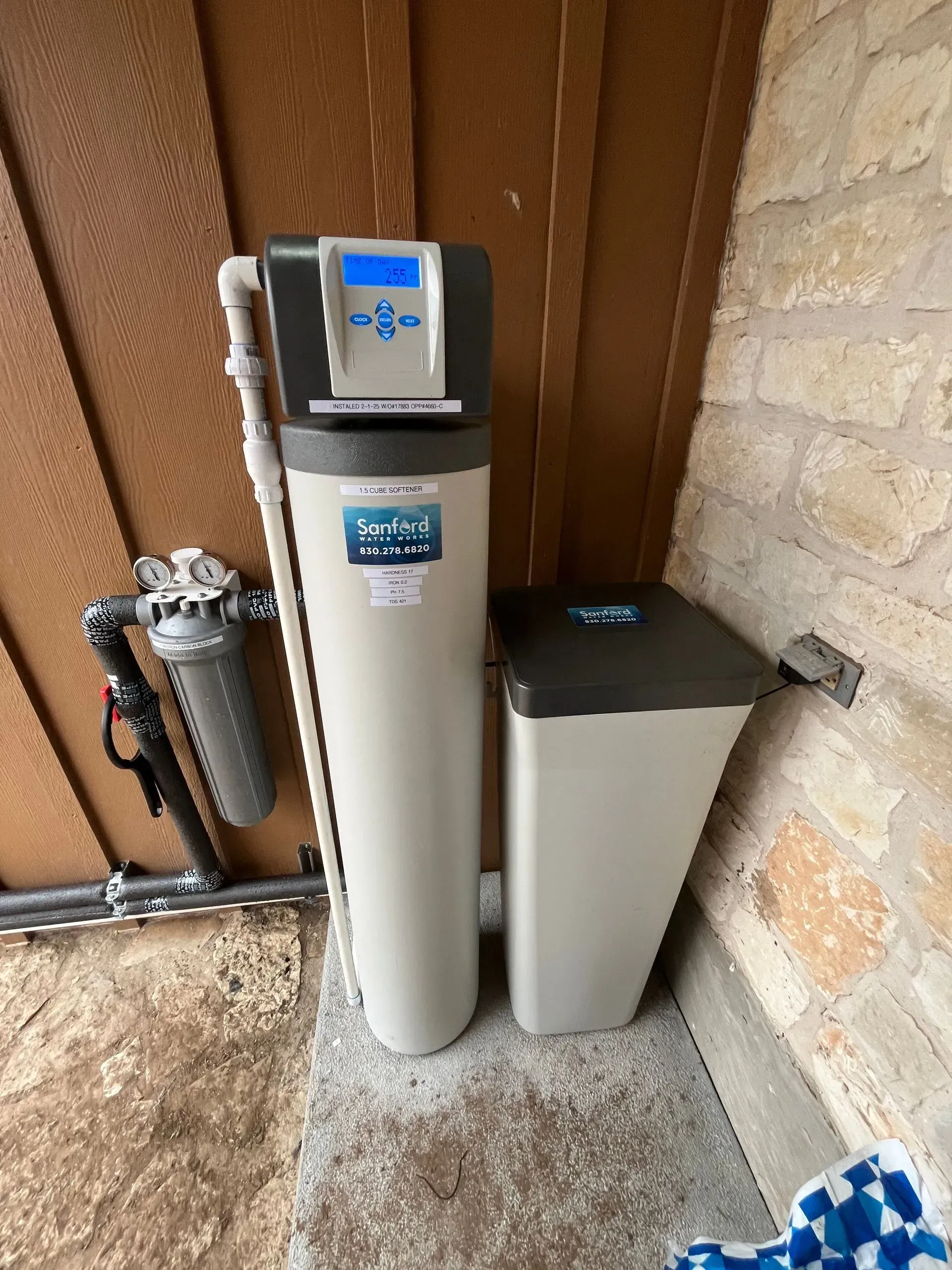 Water filtration system with two beige tanks and a digital display, against a wooden and stone wall.