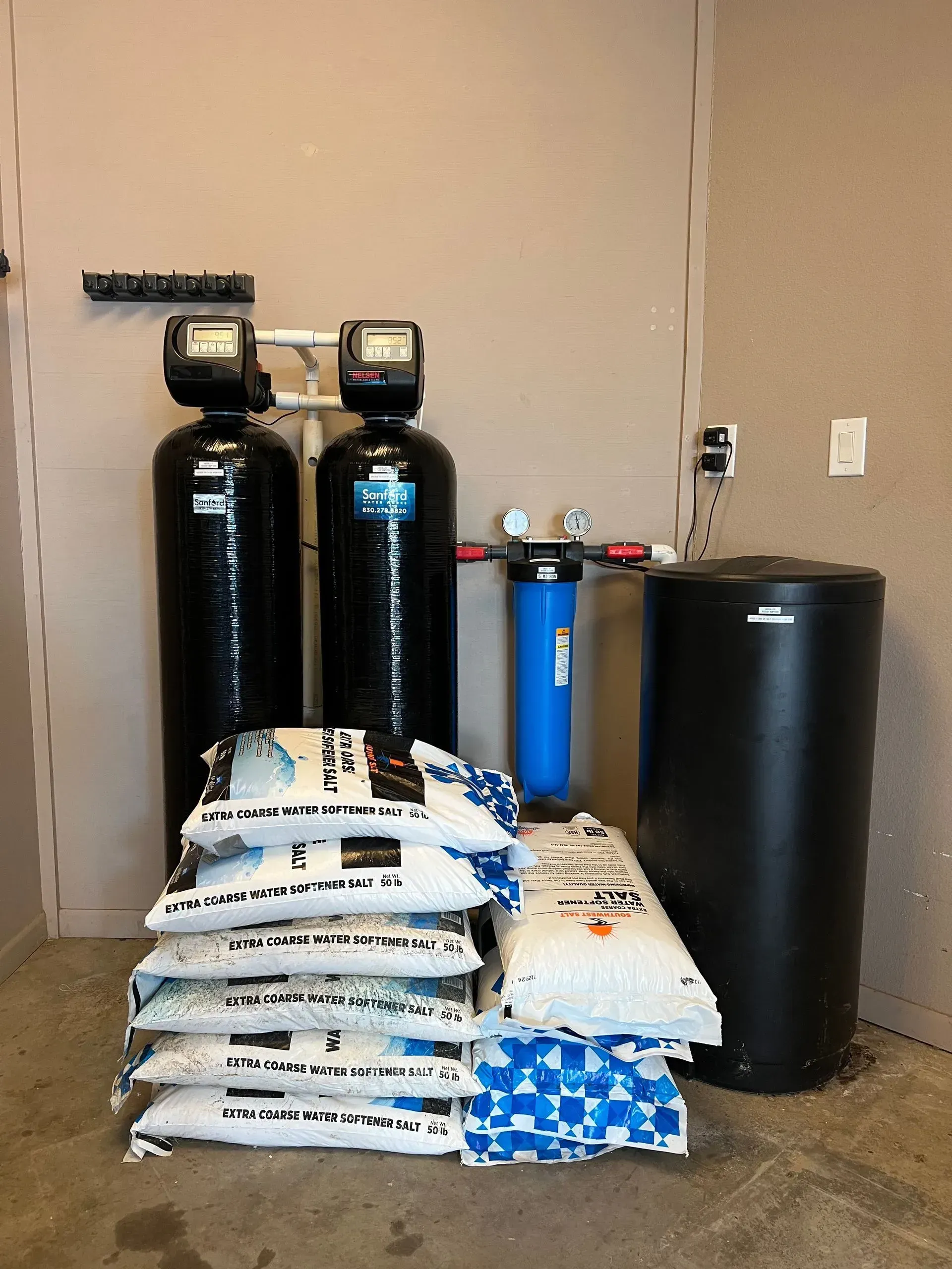Water filtration system with tanks, filter, and salt bags in a room.