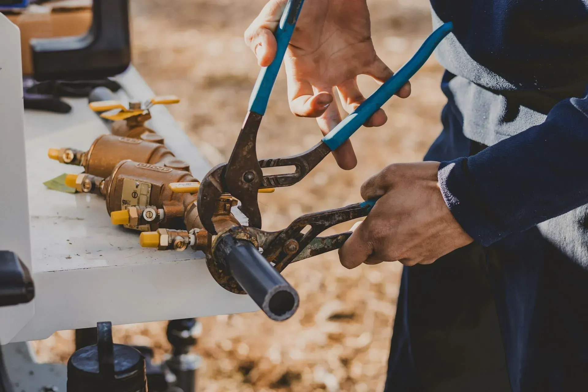 Person using pliers to work on plumbing fixtures outdoors.