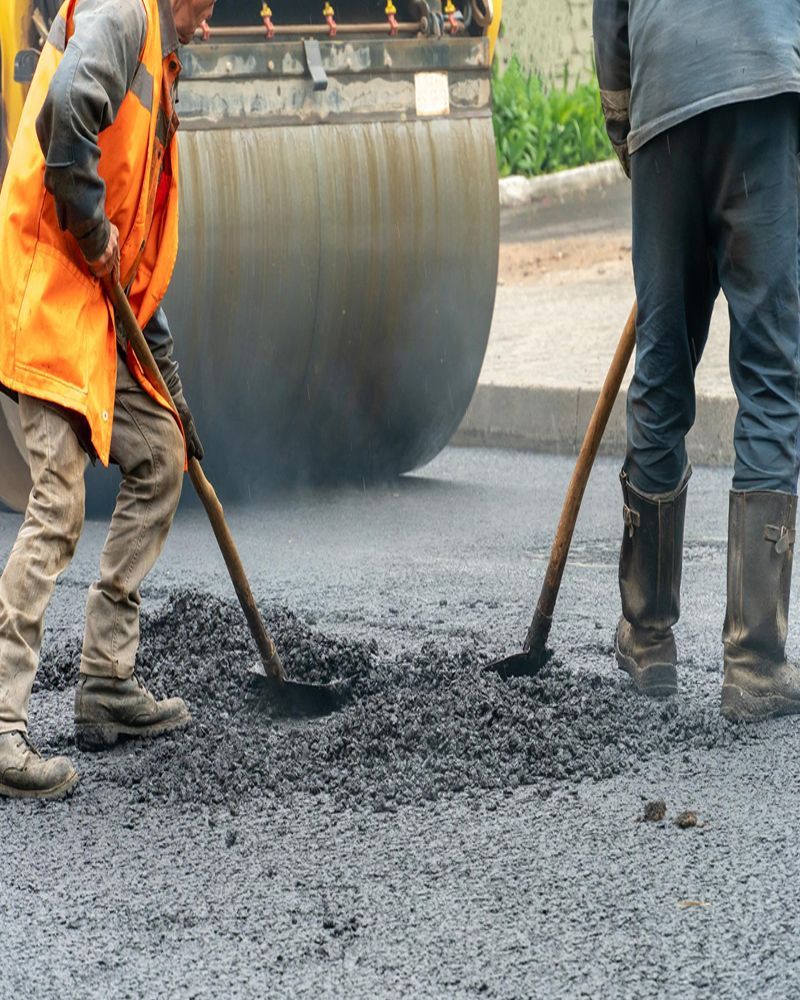 Two men are working on a road with shovels and a roller