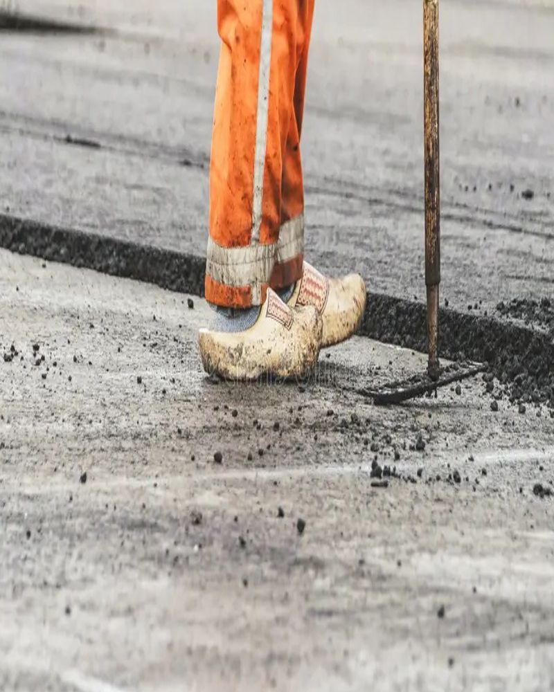 A person wearing clogs is standing on a concrete surface holding a shovel.