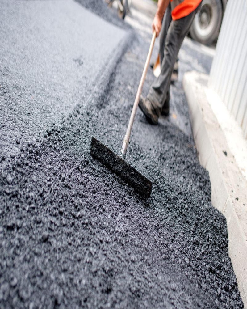 A man is spreading asphalt on the ground with a broom.