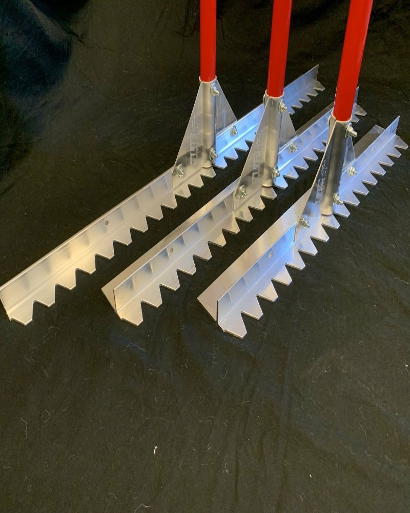 Three metal rakes with red handles on a black surface