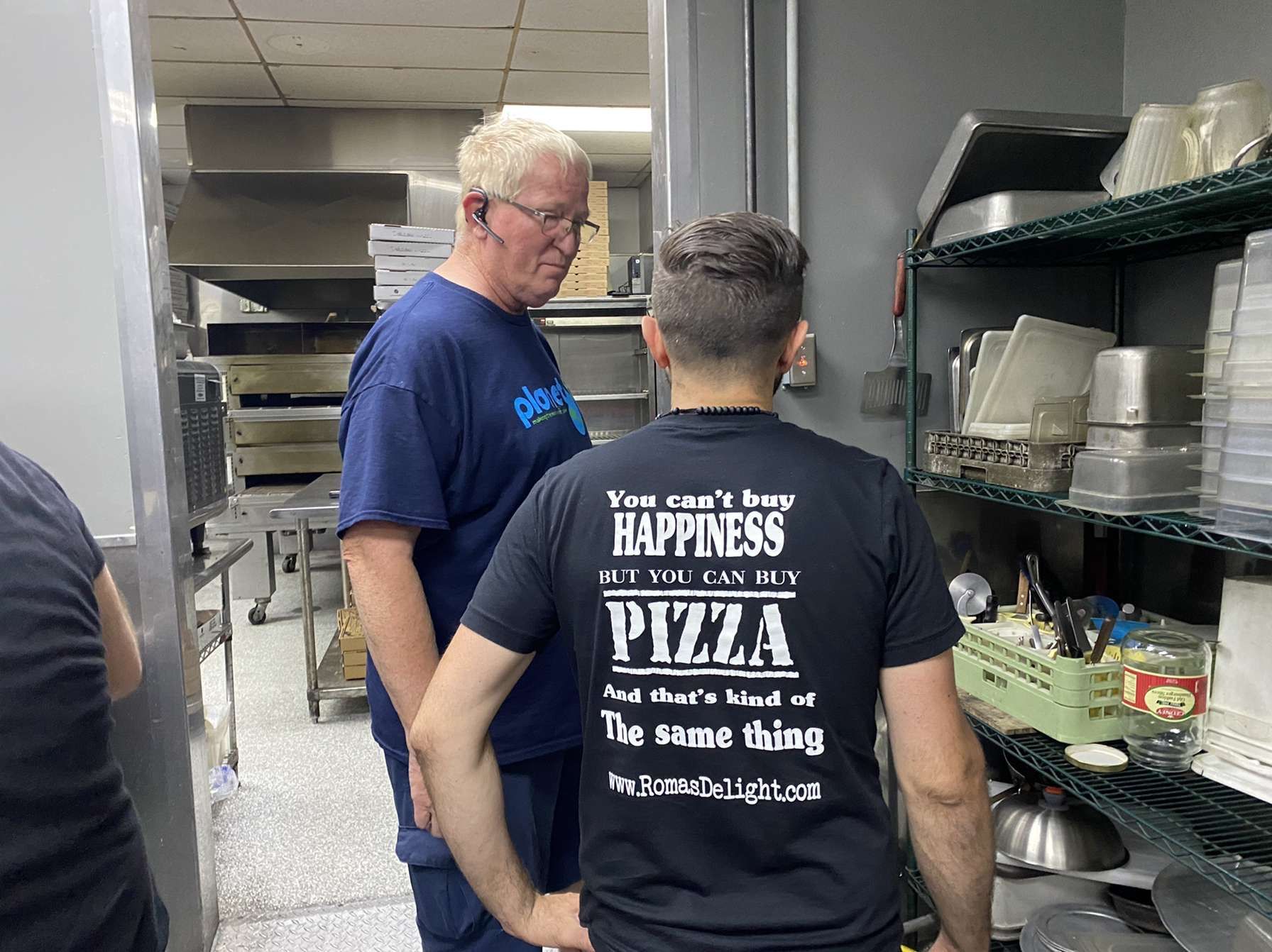 Two men are standing in a kitchen wearing shirts that say pizza.