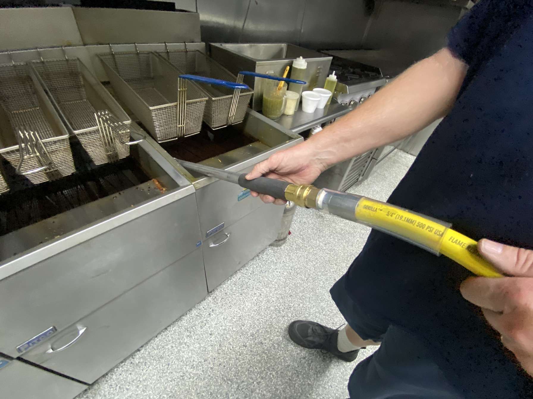 A person is holding a yellow hose in front of a fryer
