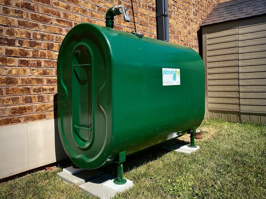 A green water tank is sitting in the grass in front of a brick building.