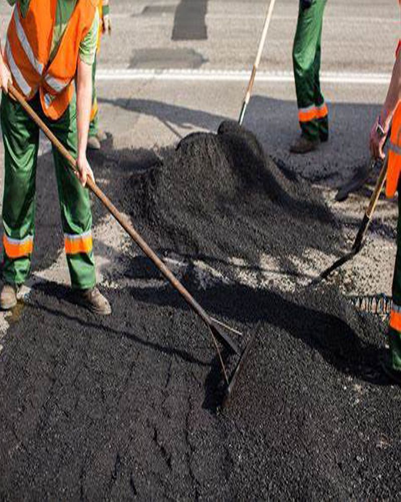 A group of people are working on a road with shovels and rakes.