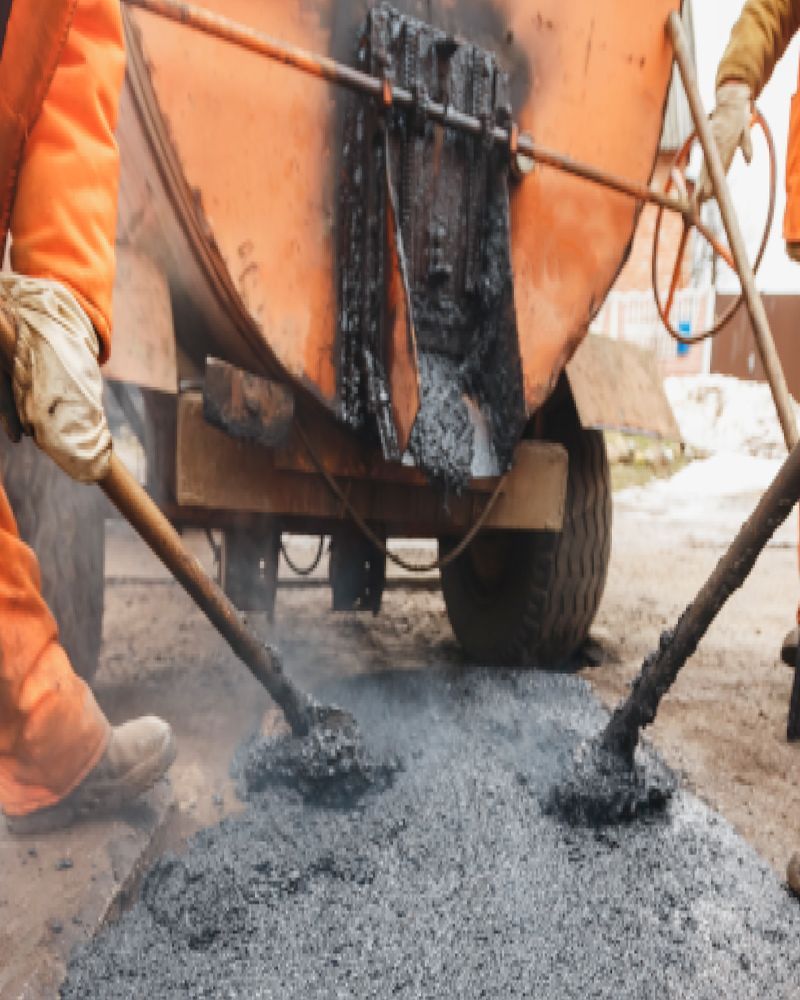 A man is pouring asphalt into a hole in the ground