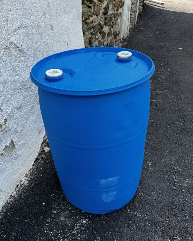 A blue plastic barrel is sitting on the side of the road