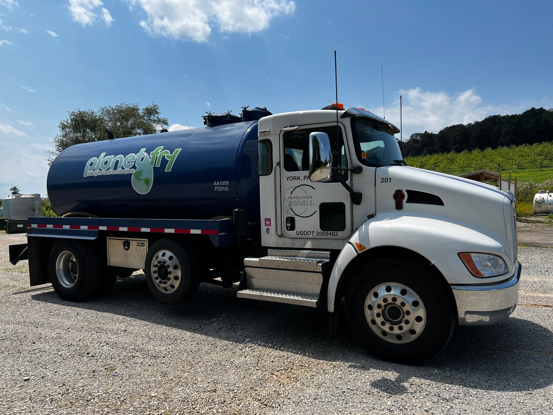 A blue and white tanker truck is parked in a gravel lot