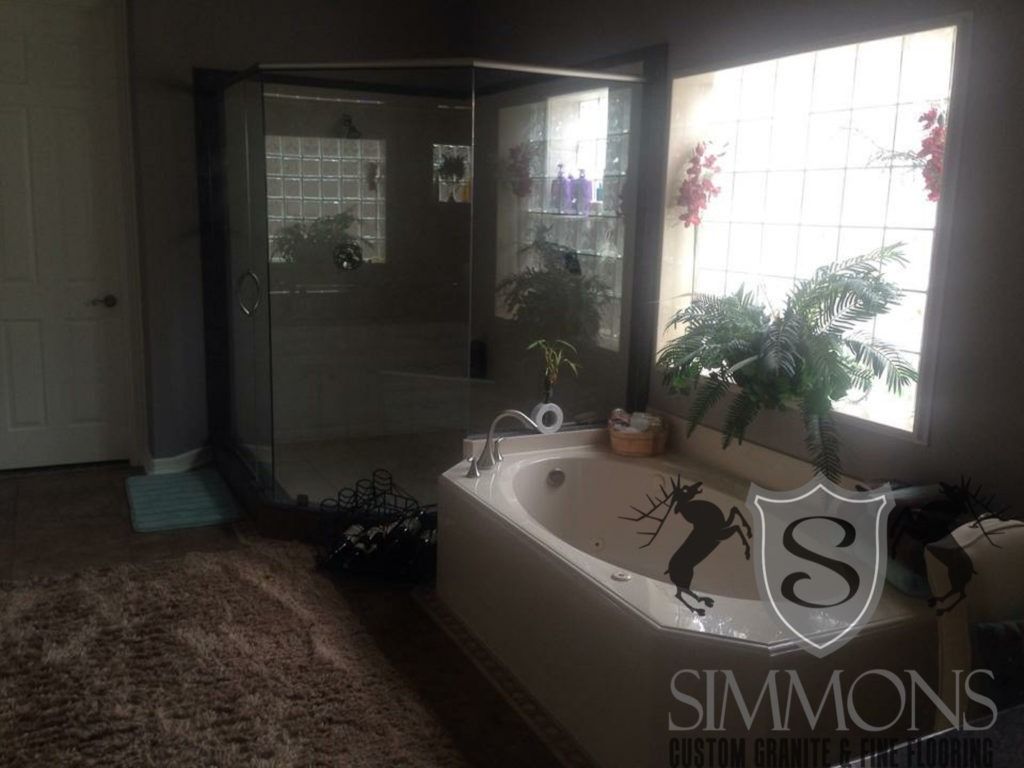Sunlit bathroom with bathtub, plants on the windowsill, and dark bath mat on the floor
