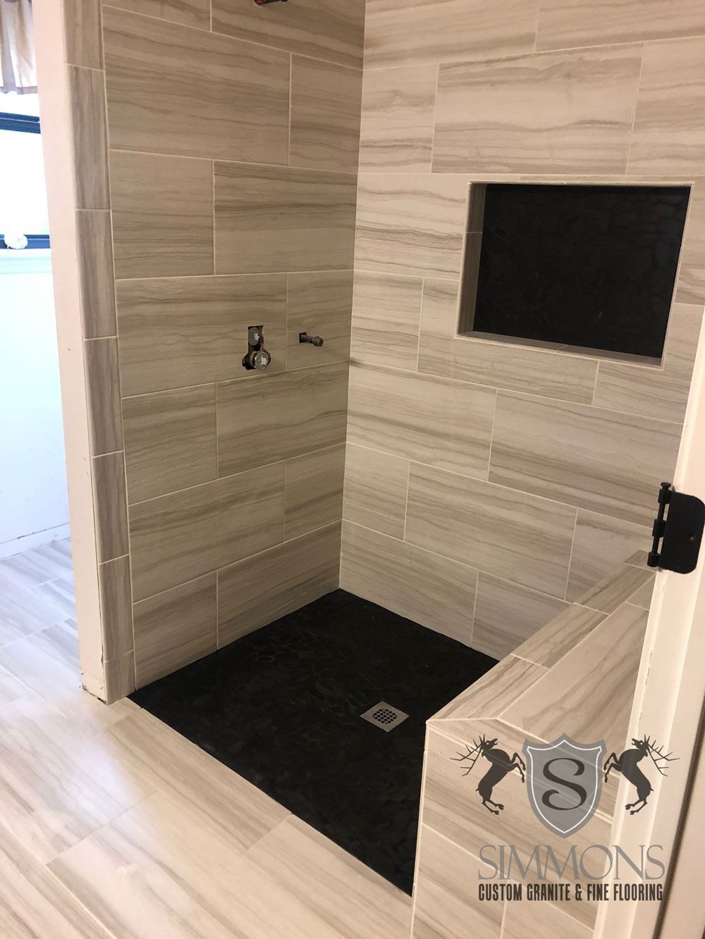 Modern bathroom shower nook with light wood tiles, black shower floor, and recessed wall niche.