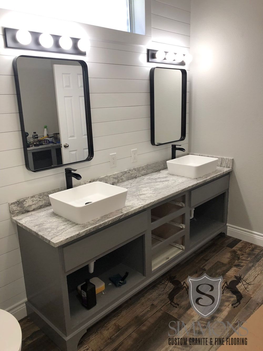 Modern bathroom vanity with two sinks, mirrors, and bright wall lights above a gray marble counter.