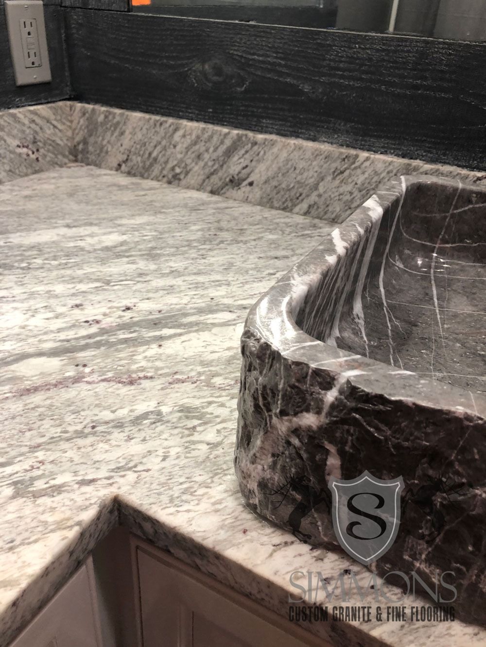 Dark marble bathroom countertop with an integrated sink and backsplash near a corner wall.