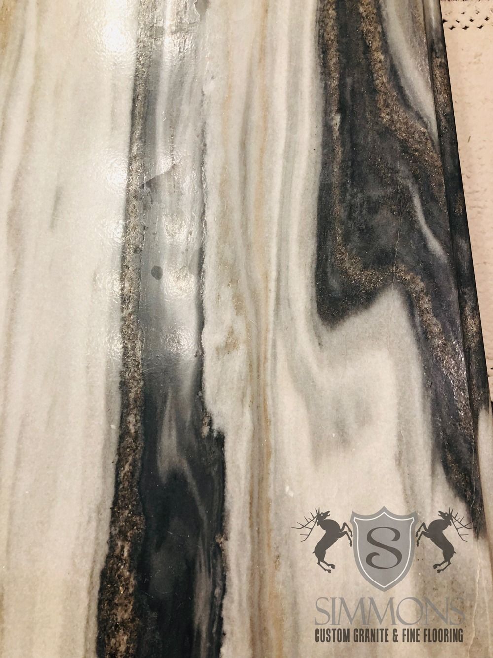 Abstract beige and black marble-like stone pattern with a small logo near the bottom right