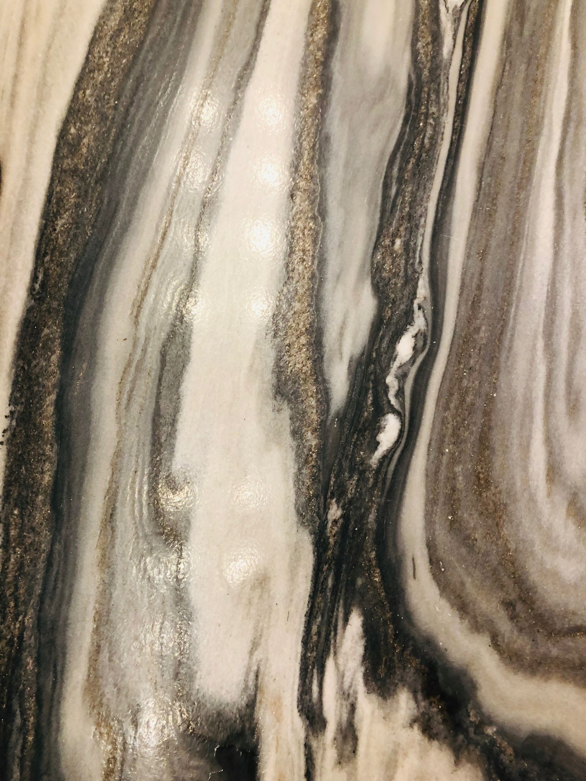 Beige, gray, and black marbled stone pattern with flowing vertical veins