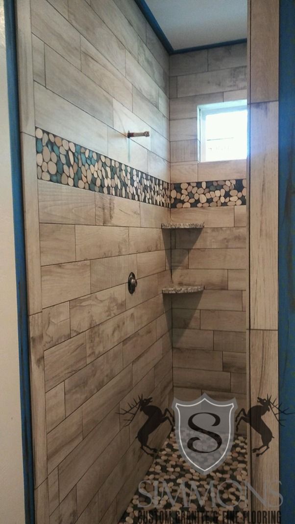 Stone-tiled shower with decorative border, corner shelf, and window above a showerhead and faucet.