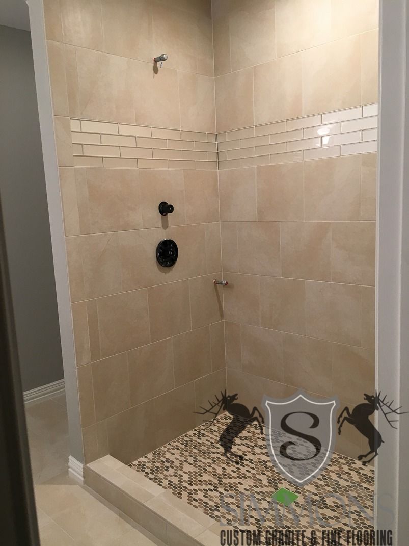 Beige tiled shower stall with pebble floor, wall niches, and plumbing fixtures.