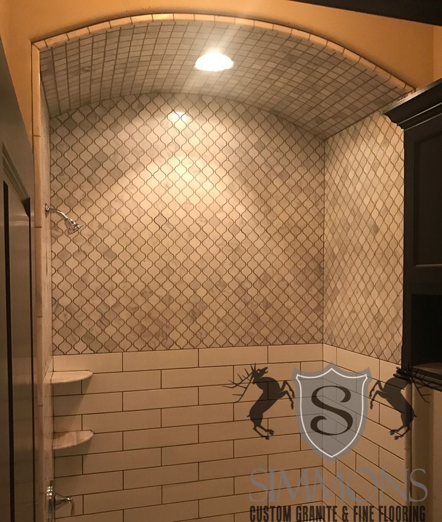 A tiled shower stall with a rounded tiled alcove, overhead light, and a shelf on the left side.