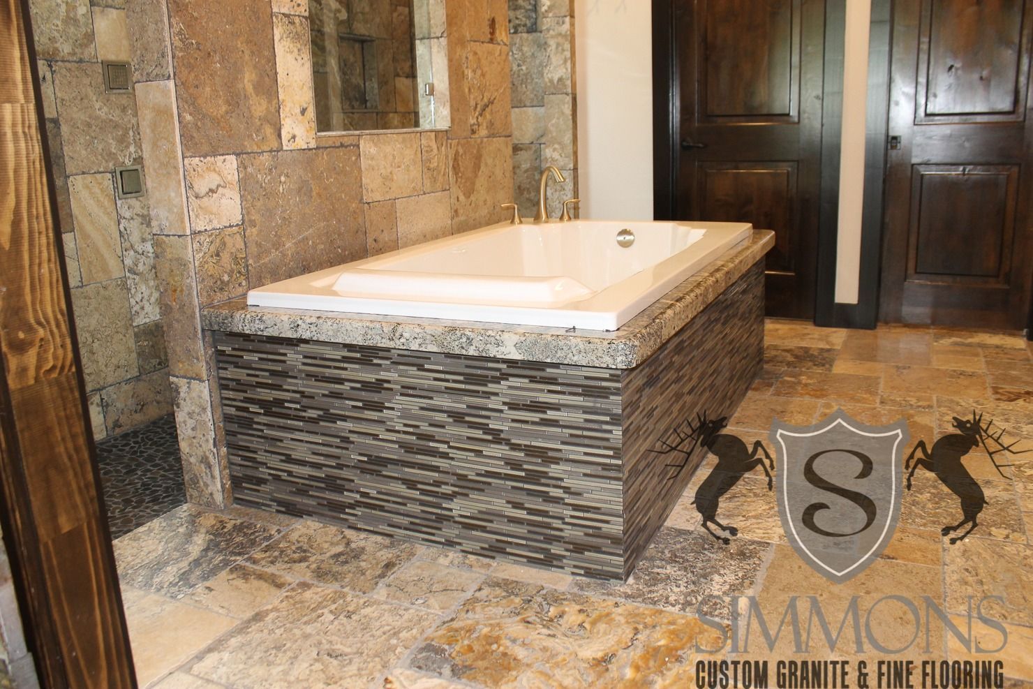 Stone bathroom vanity with white countertop, rustic tile walls, and dark wooden doors