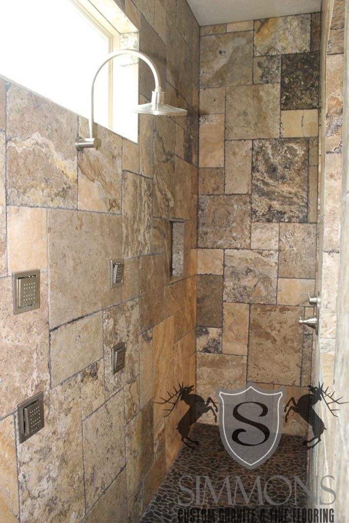 Stone-tiled shower with glass window and dark fixtures, showing a small shower bench in the corner