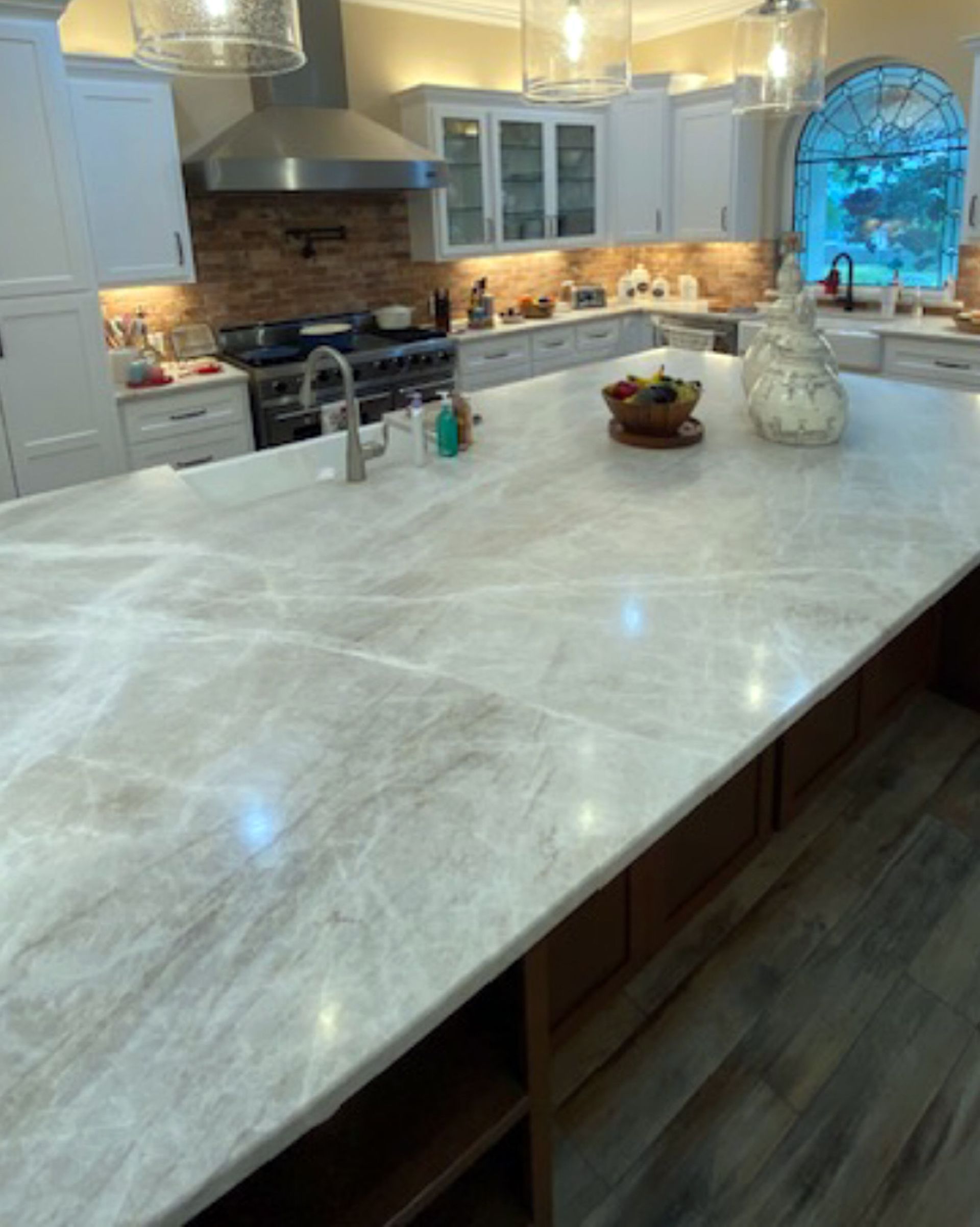 Bright kitchen with a large marble island, white cabinets, and a blue-tinted window.
