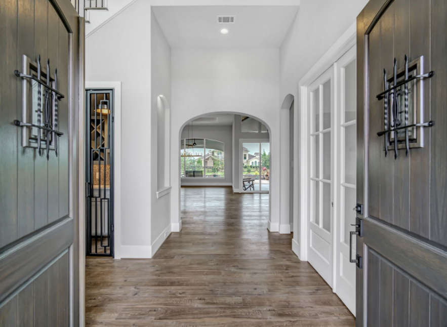 Front entry hallway with open double doors, wood floors, white walls, and an arched opening to a bright room
