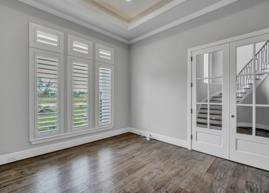 Empty gray room with wood floors, white shutters, and French doors by a staircase