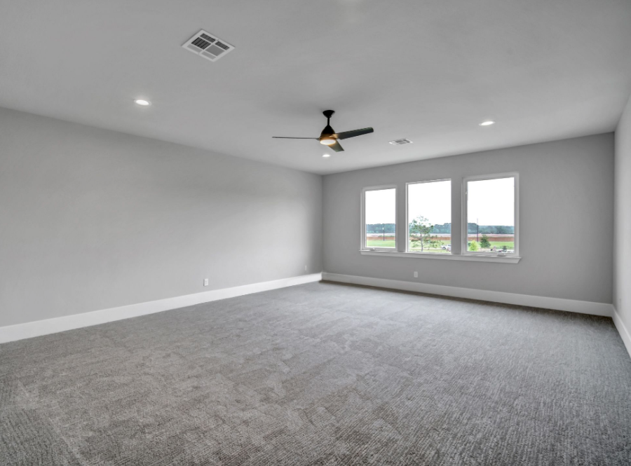 Empty gray bedroom with carpet, recessed lights, ceiling fan, and three windows.
