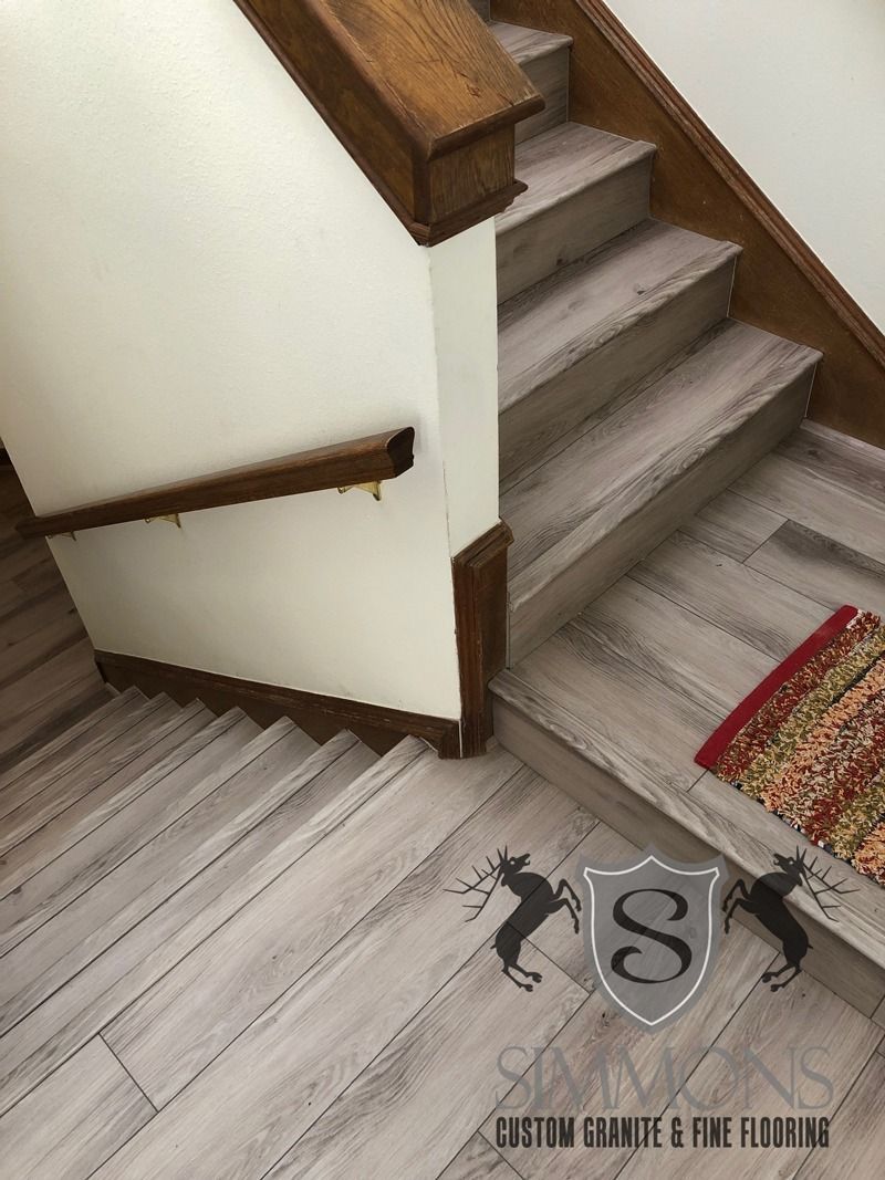 Stairwell with gray steps, white walls, wooden handrails, and a small rug at the landing.