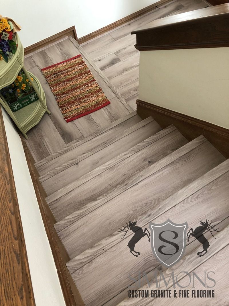 Diagonal view down a light wood staircase with a floral runner and dark handrail, seen from the top landing.