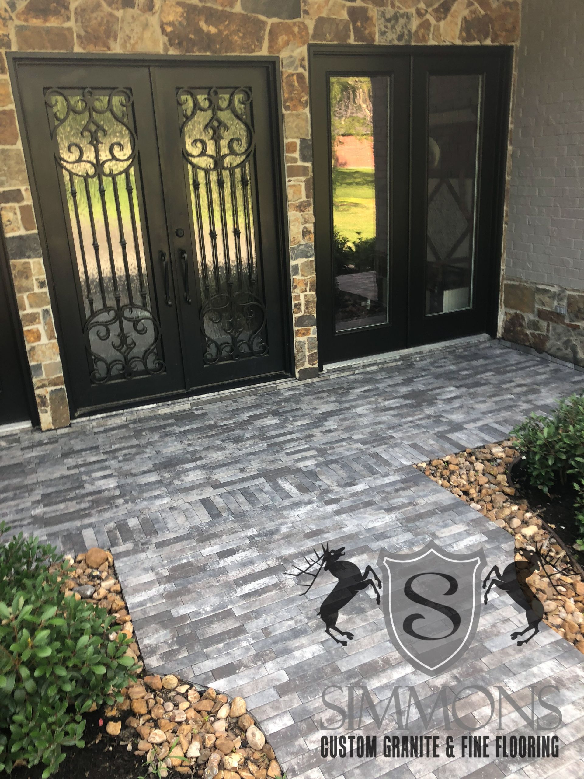 Stone front entry with double black wrought-iron doors and a gray paver walkway leading to a house entrance