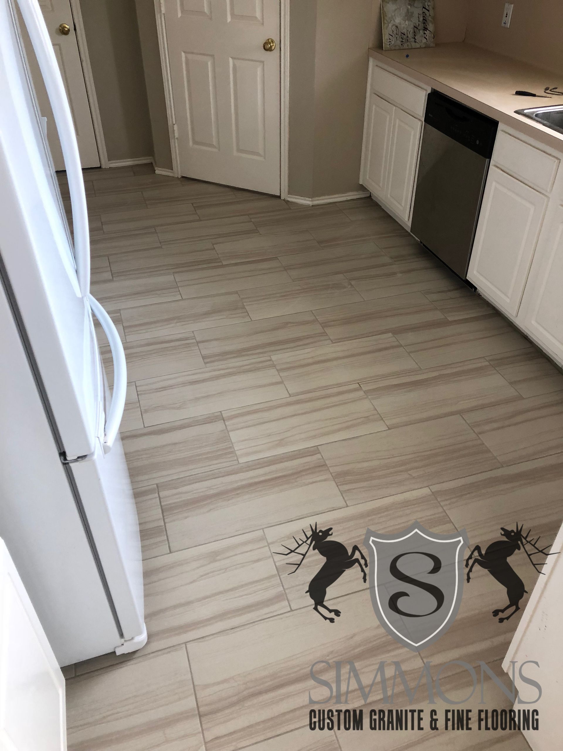 Light wood kitchen floor with white cabinets, black dishwasher, and a logo watermark near the bottom.