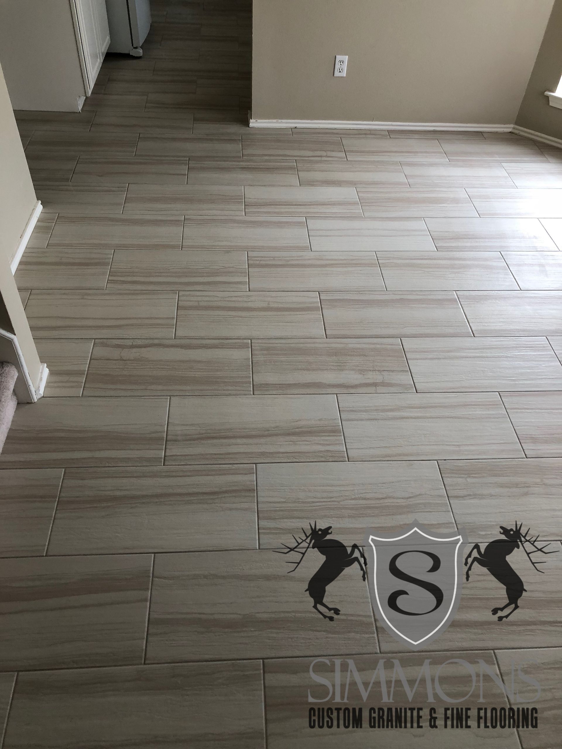 Empty room with light gray wood-look tile flooring and beige walls, viewed toward a hallway.