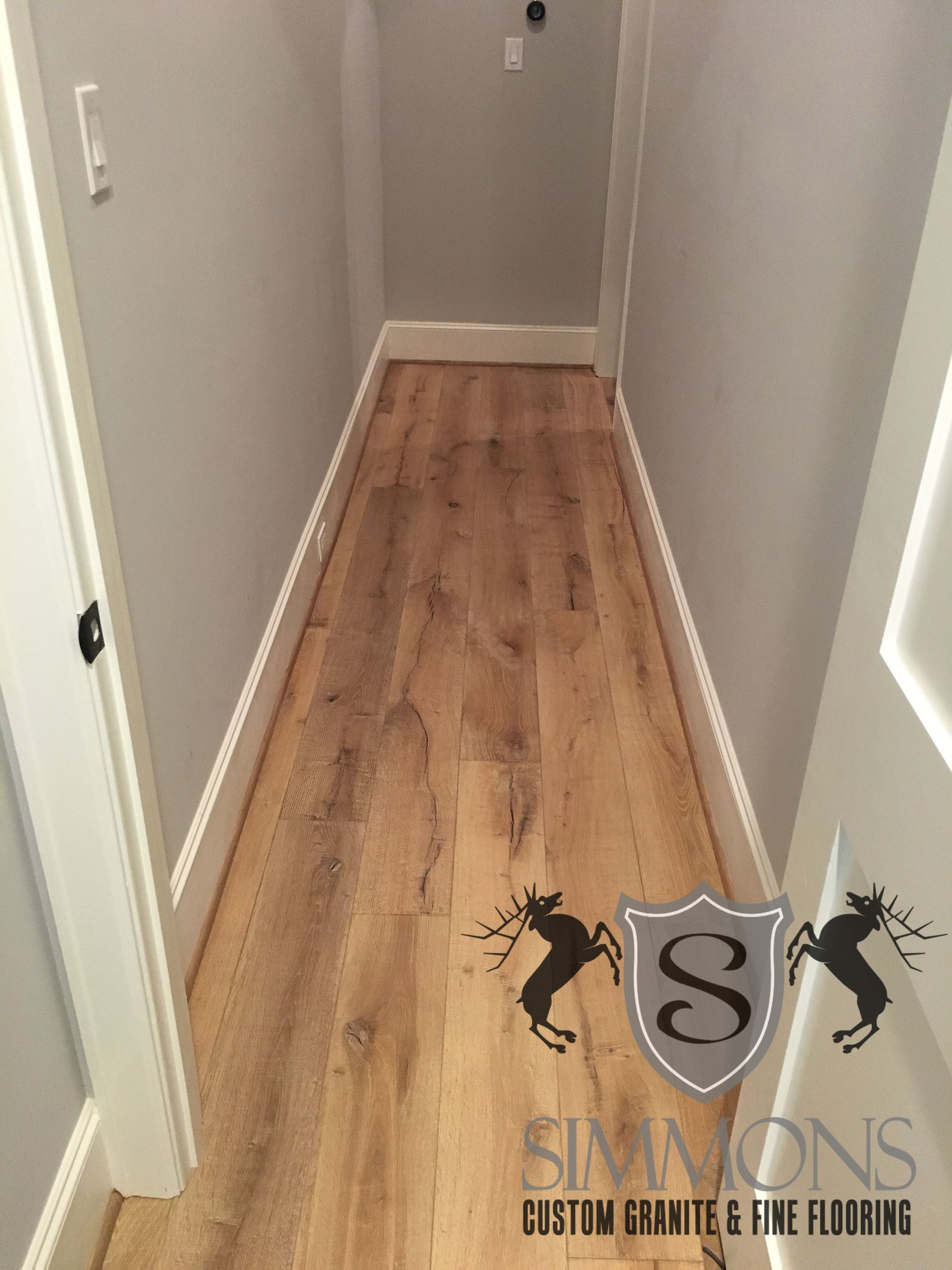 Narrow hallway with light wood floor, white walls, and a white door at the end.