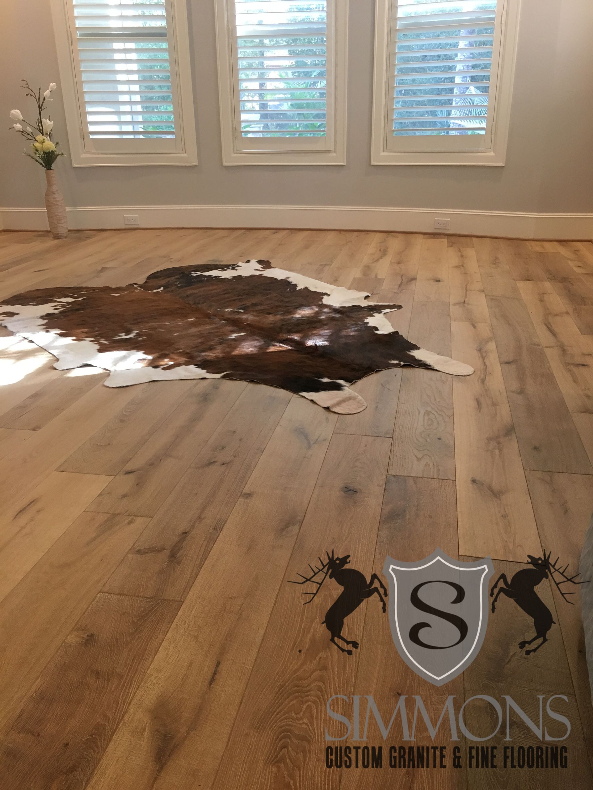 Damaged hardwood floor with a large dark stain and scattered debris near a windowed wall.