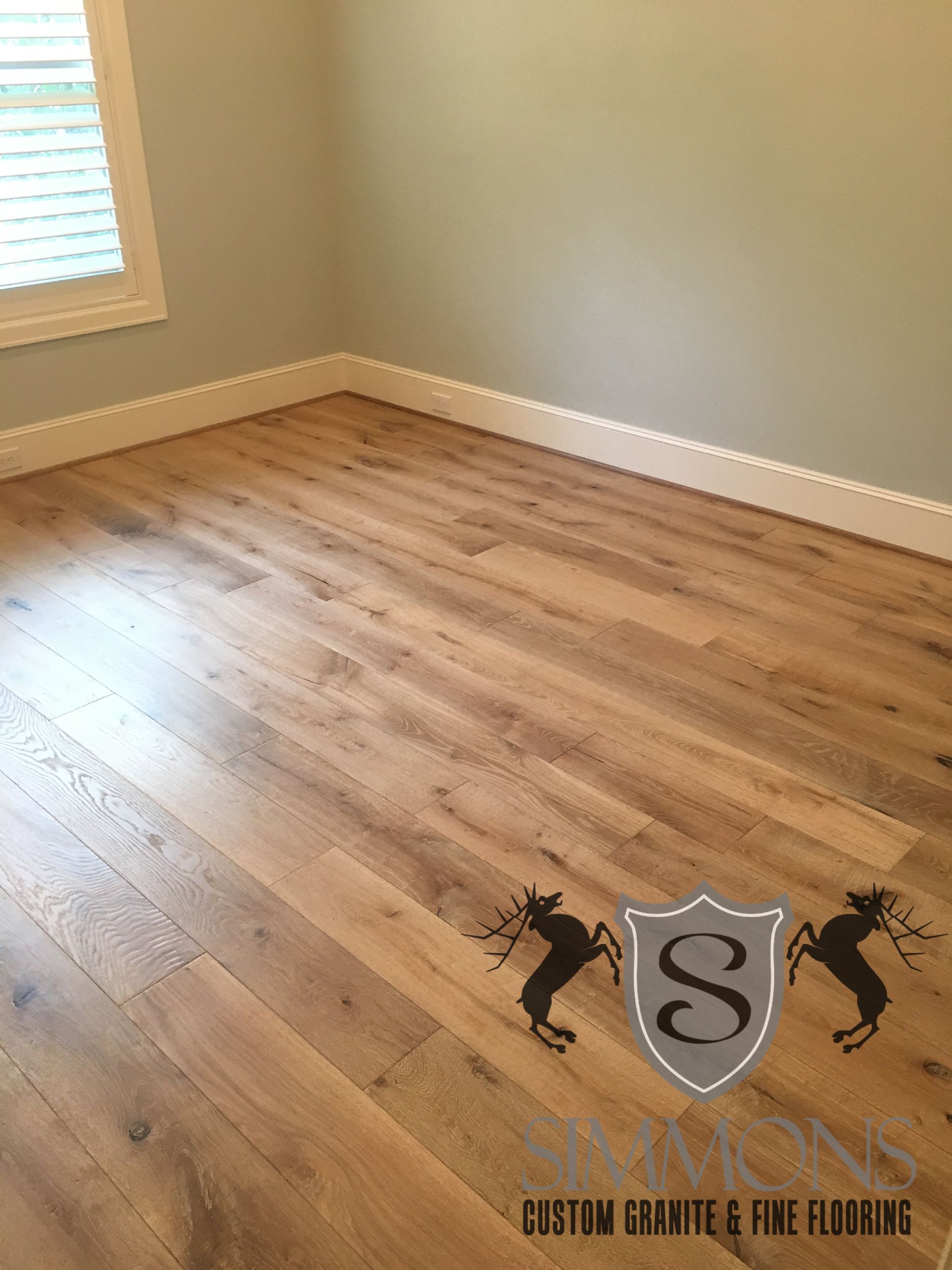 Empty room with light wood floors, gray walls, and a window with blinds.