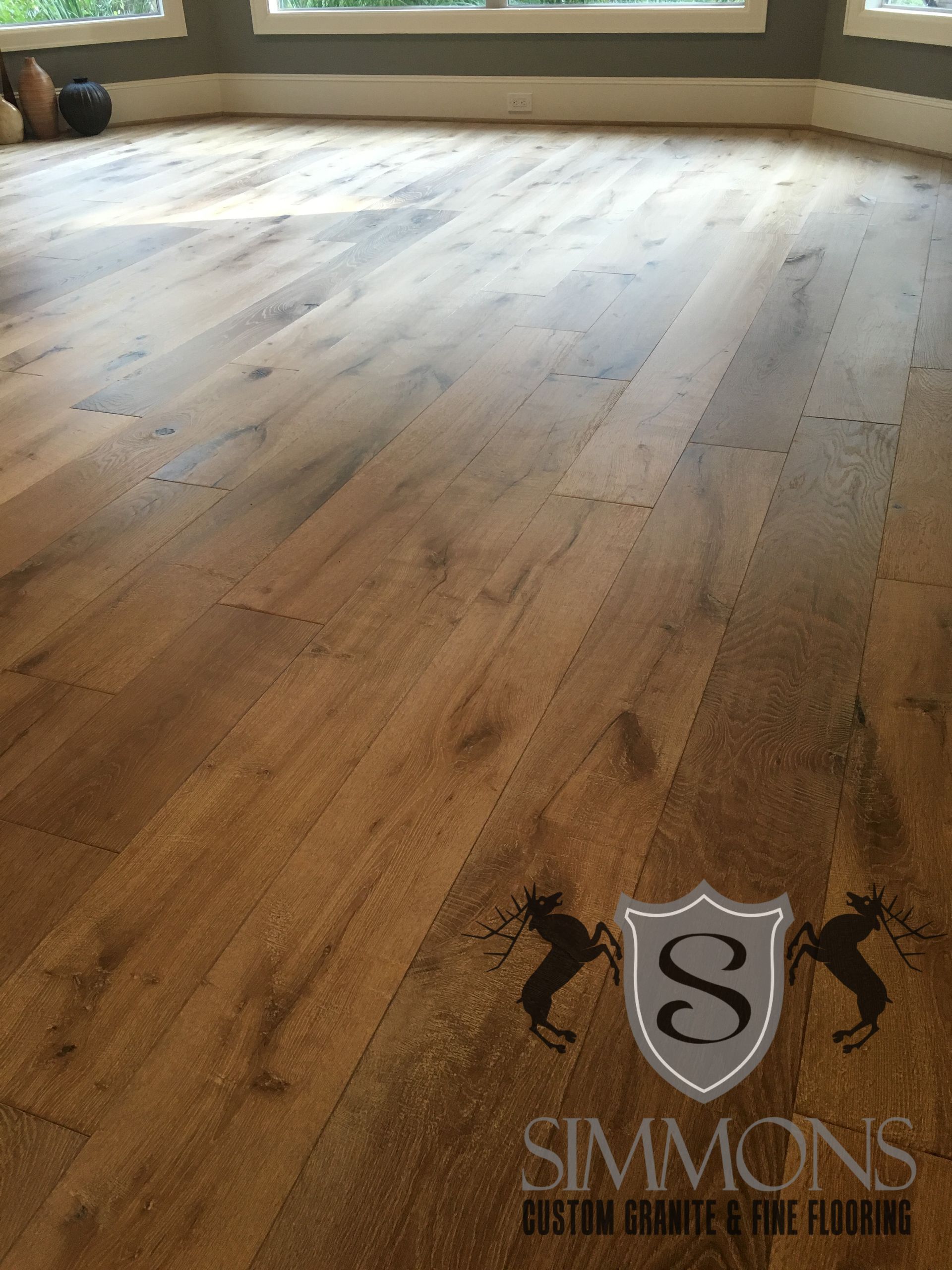 Empty sunlit room with wide wood plank flooring and large windows; Simmons logo watermark at bottom right