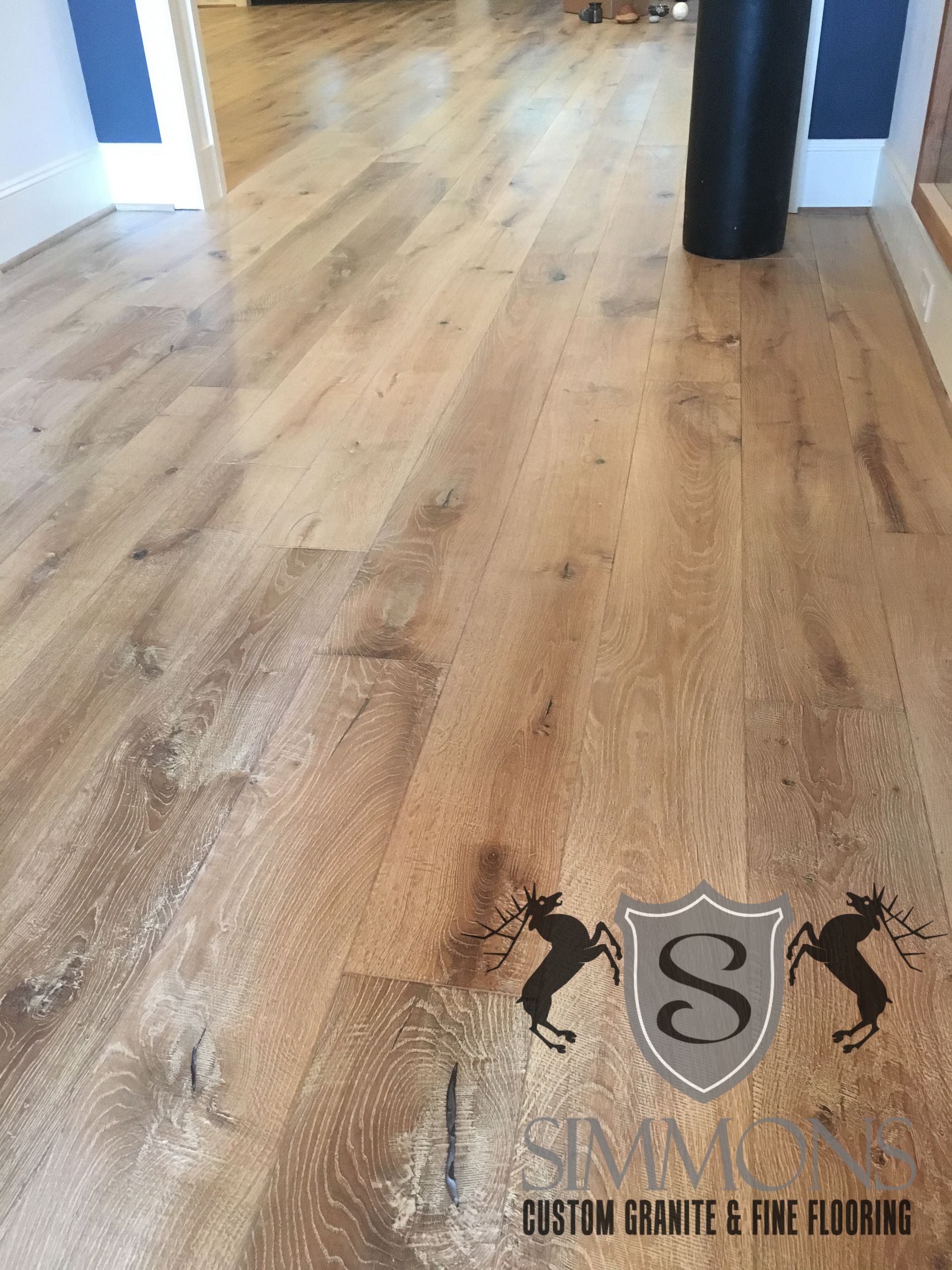Light wood floor in an indoor hallway with black columns and a watermark near the bottom.