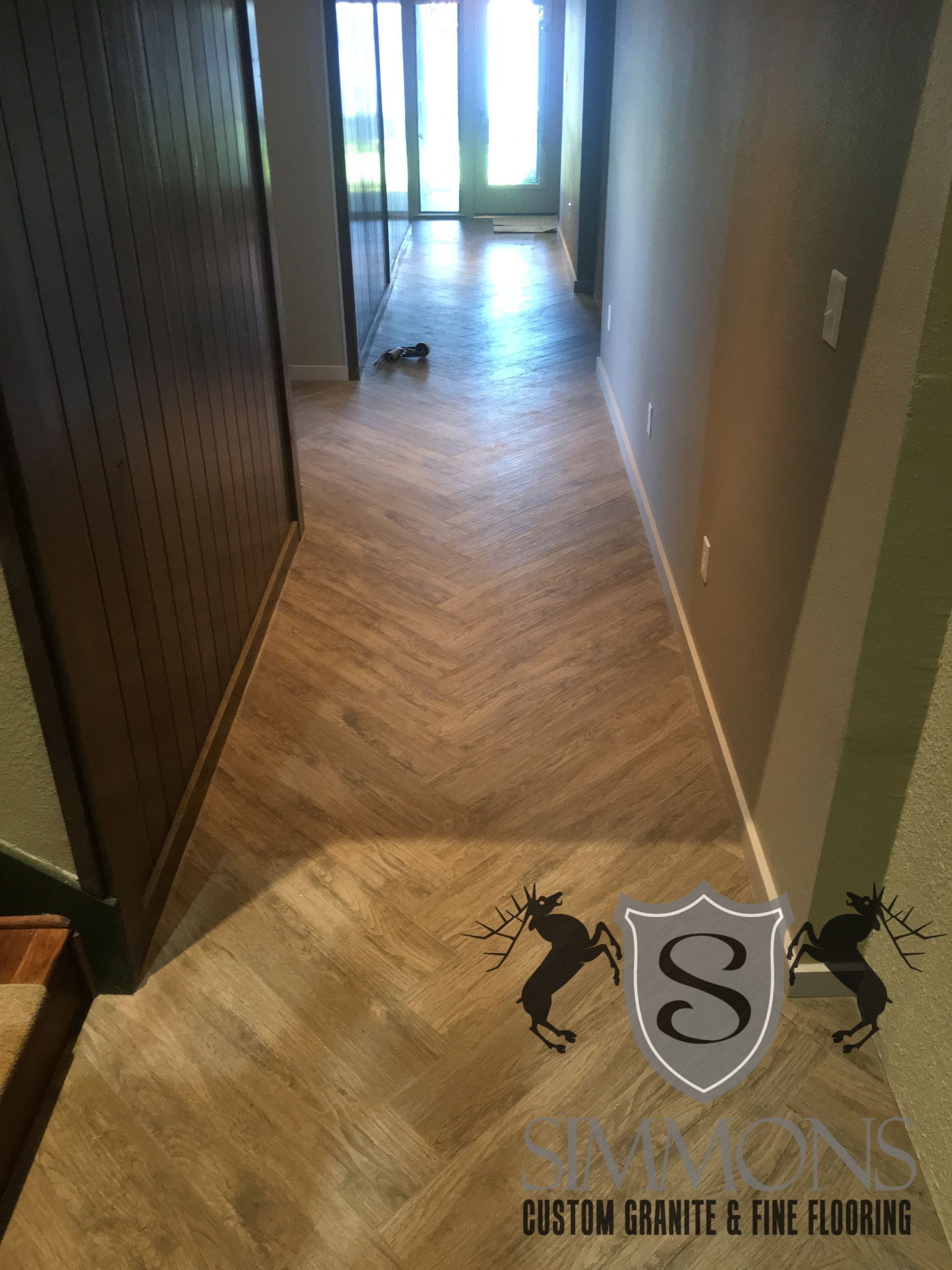 Narrow apartment hallway with wood flooring leading to a bright doorway and a glass patio door.
