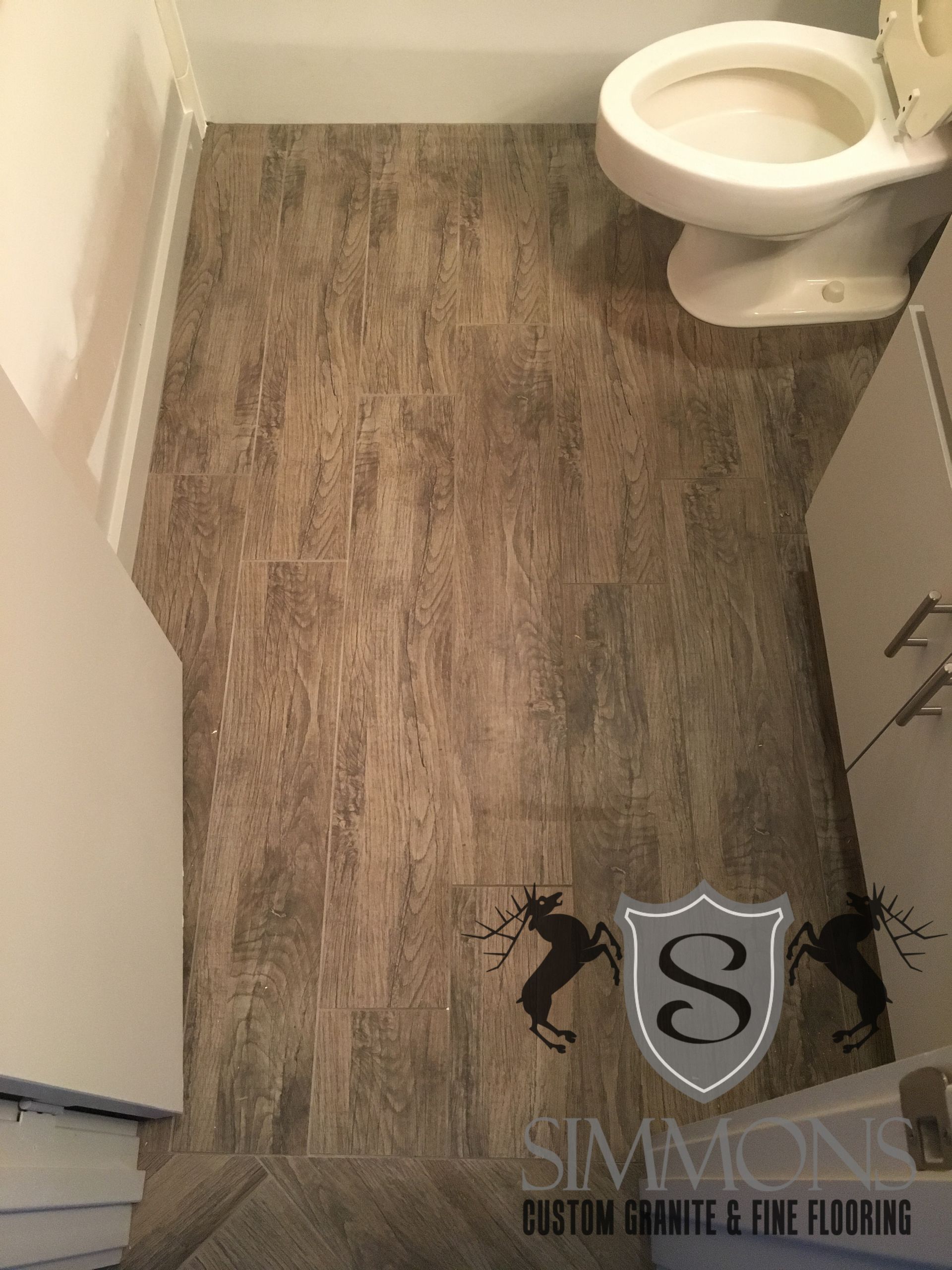 Small bathroom with wood-look flooring, white toilet, and vanity cabinets.
