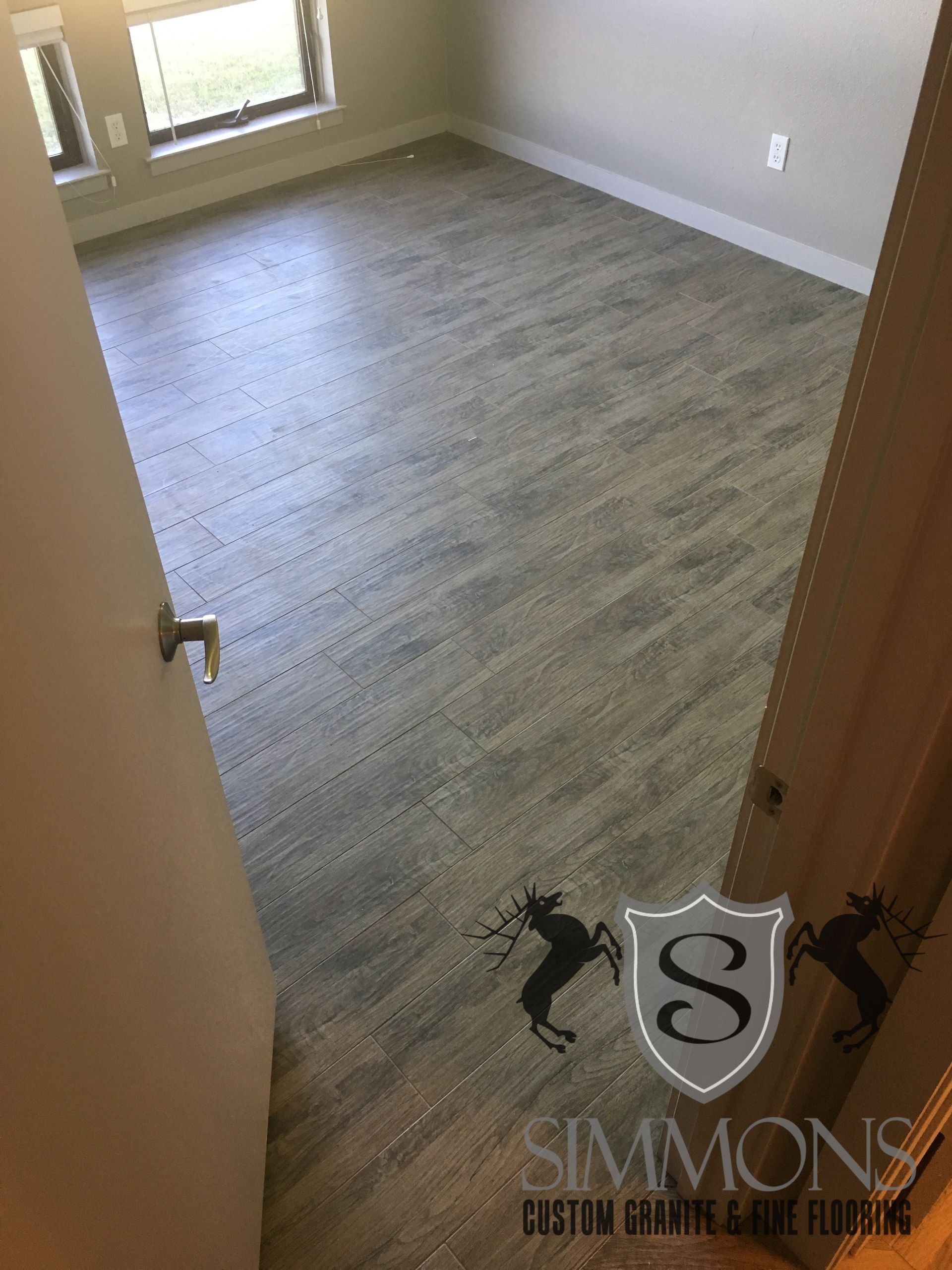 Empty beige bedroom with gray carpet, viewed through a doorway and lit by a window.