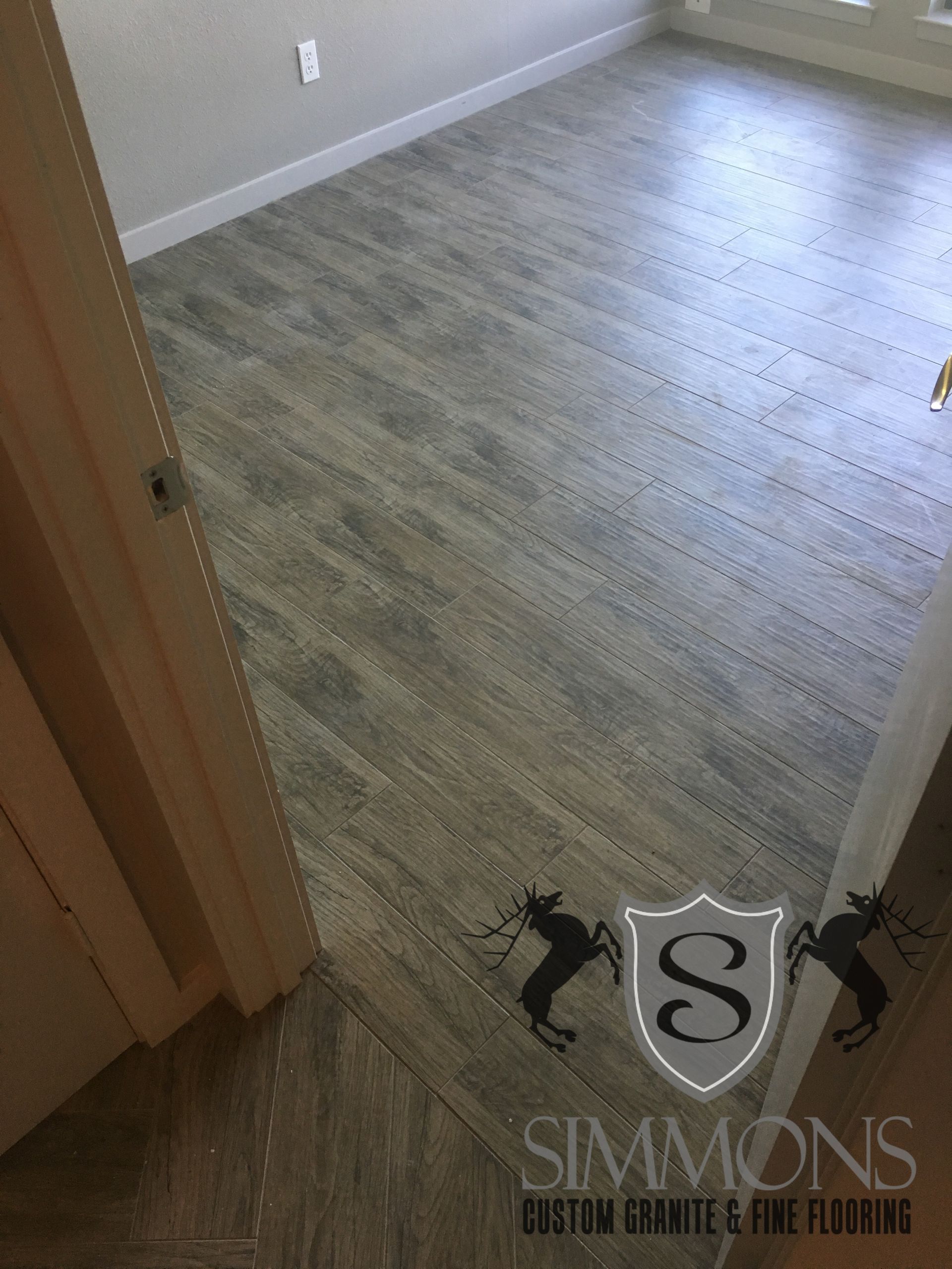 Empty room with gray wood-look flooring, beige walls, and a doorway in the foreground.