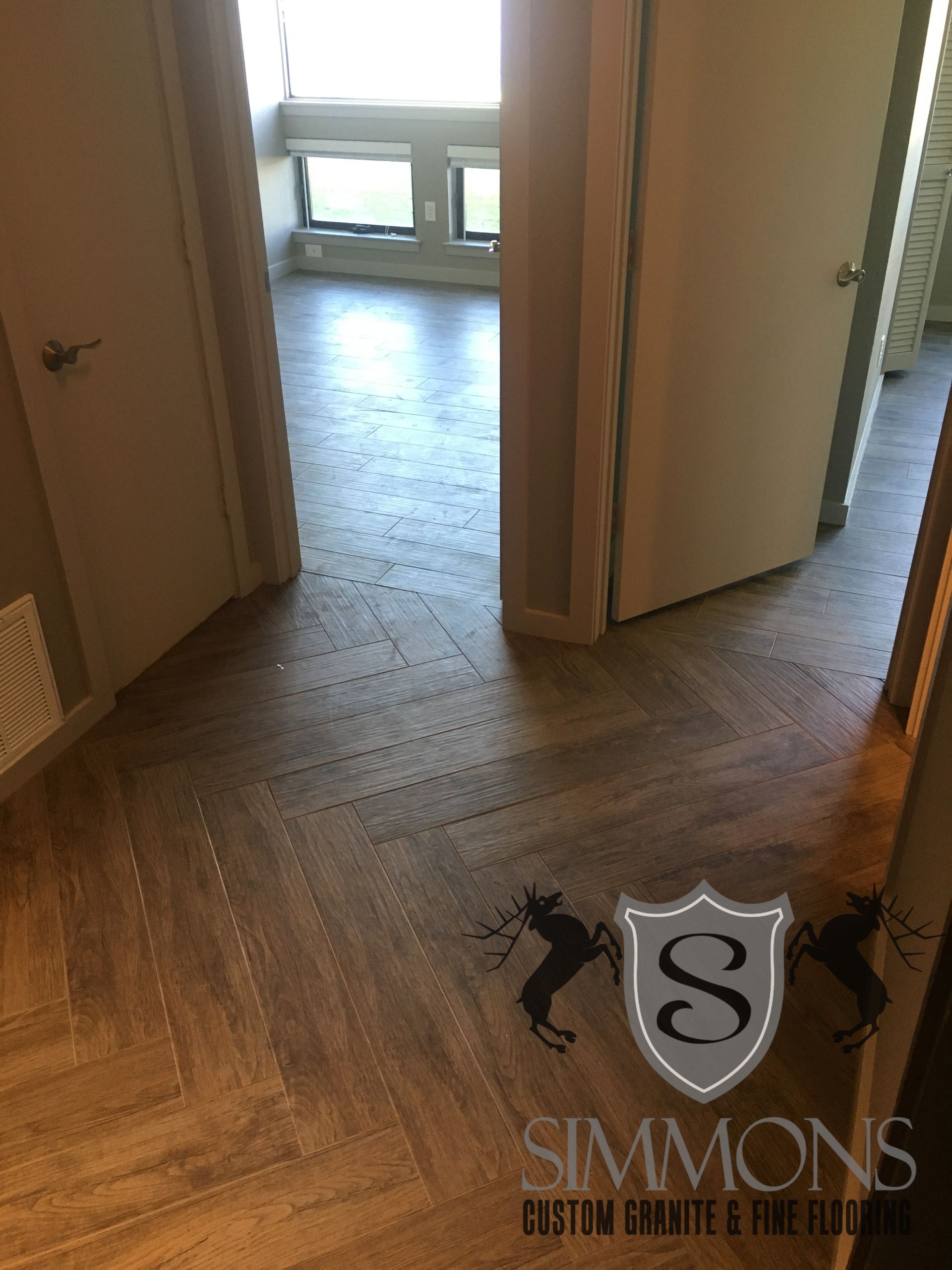 Empty hallway with herringbone wood floor leading to a bright room with windows.