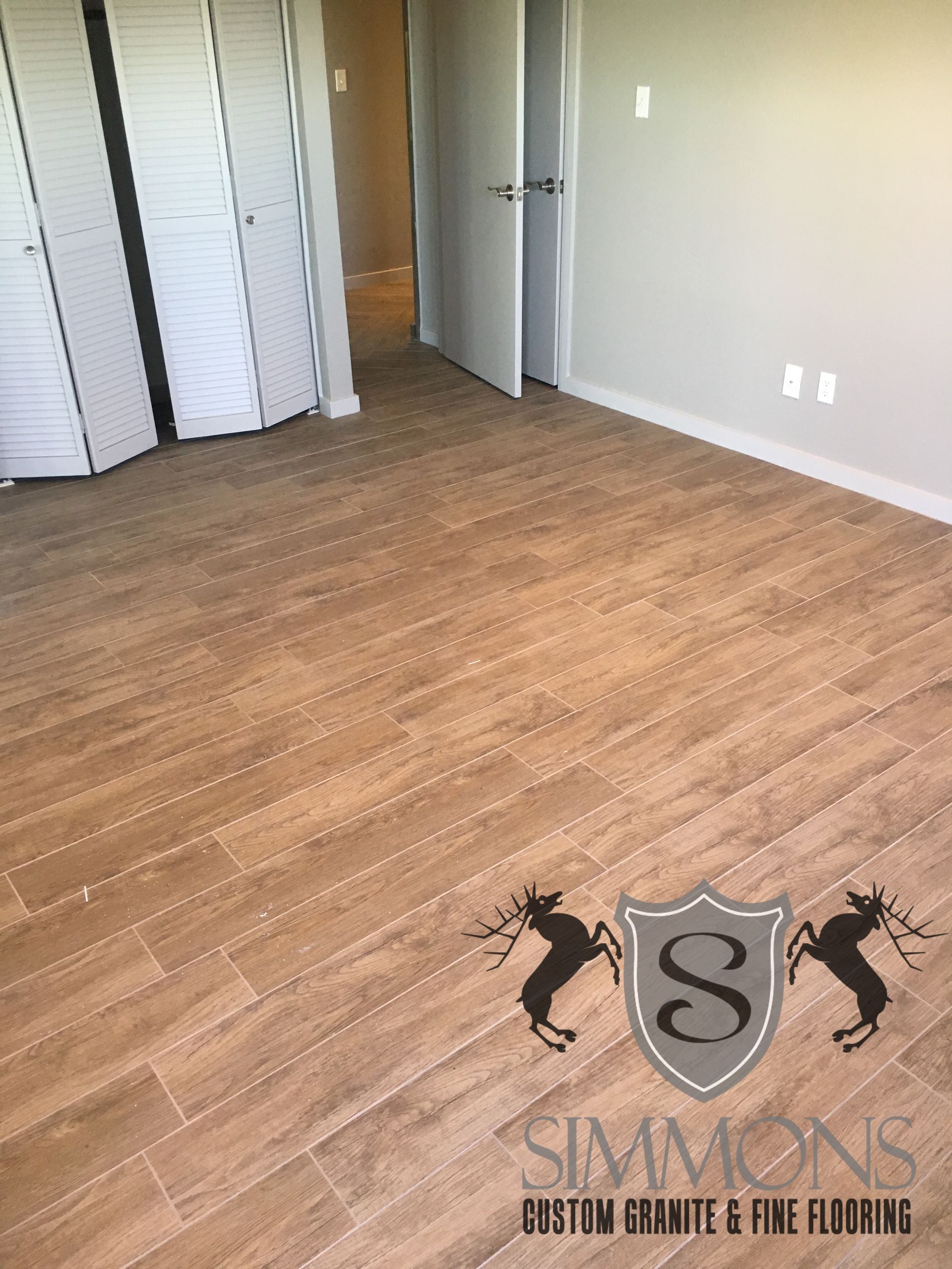 Empty beige bedroom with wood flooring, open closet doors, and a doorway on the right.